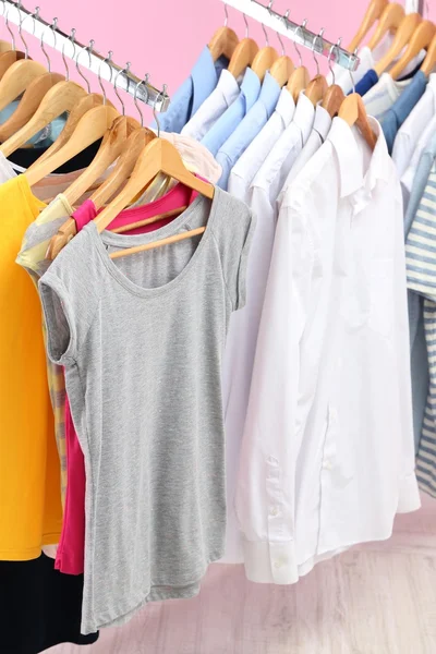 Verschillende kleding op hangers, op roze achtergrond — Stockfoto