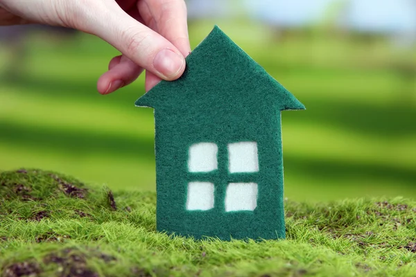 Petite maison en papier à la main sur herbe verte sur fond lumineux — Photo