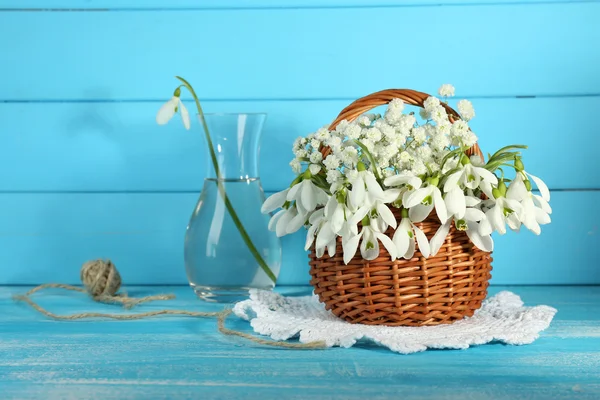 Hermosas gotas de nieve en cesta sobre mesa de madera azul —  Fotos de Stock