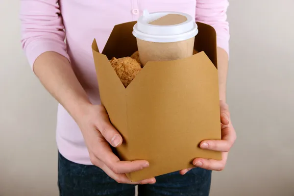 Woman holds box with coffee and cookies on grey background — Stock Photo, Image