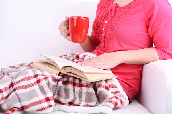 Woman sitting on sofa,  reading book and  drink coffee or tea, close-up — Stock Photo, Image