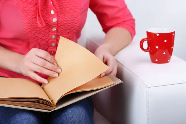 Mulher sentada no sofá, lendo livro e beber café ou chá, close-up — Fotografia de Stock