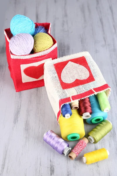 Bolsas con bobinas de hilo de colores y bolas de lana sobre fondo de madera — Foto de Stock
