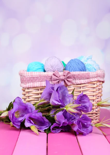 Purple artificial eustoma and woolen balls of yarn in basket on light background — Stock Photo, Image