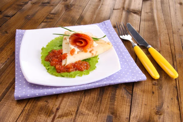 Pannenkoek met zalm, rode kaviaar en mayo, groene ui, op plaat, op kleur servet, op houten achtergrond — Stockfoto