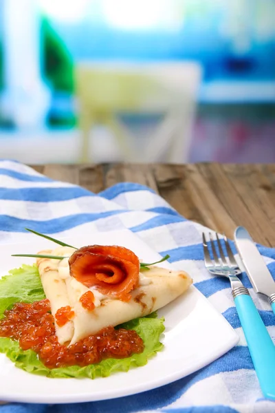 Pancake con caviale rosso, salmone e maionese, cipolla verde, su piatto, su tovagliolo di colore, su tavolo di legno, su sfondo brillante — Foto Stock