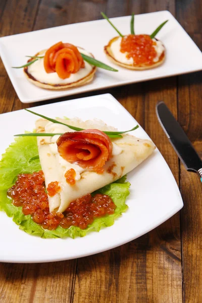 Panquecas com caviar vermelho, salmão e maionese, cebola verde, no prato, no fundo da mesa de madeira — Fotografia de Stock