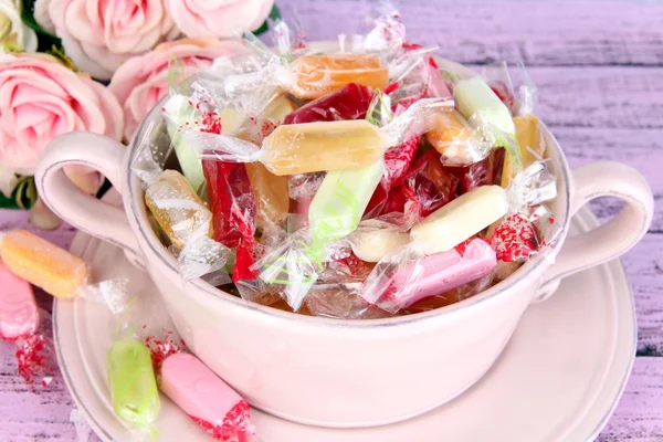 Вкусные конфеты в миске с цветами на деревянном фоне — стоковое фото