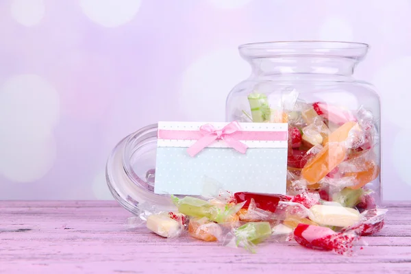 Tasty candies in jar with card on table on bright background — Stock Photo, Image