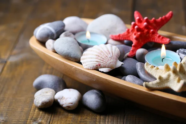 Houten kom met spa stenen, zeeschelpen en kaarsen op houten achtergrond — Stockfoto