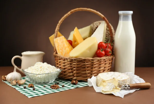 Basket with tasty dairy products on wooden table, on dark brown background — Stock Photo, Image