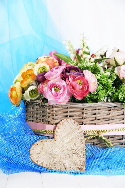 Mooie bloemen in rieten mand, op kleur weefsel en houten achtergrond — Stockfoto