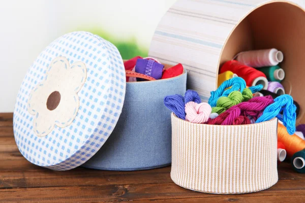 Cajas decorativas con madejas coloridas de hilo y cremalleras en la mesa sobre fondo brillante — Foto de Stock
