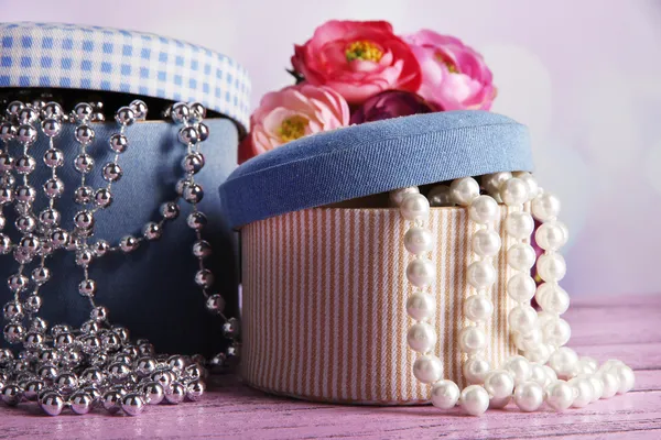 Decorative boxes with beads and flowers on table on bright background — Stock Photo, Image