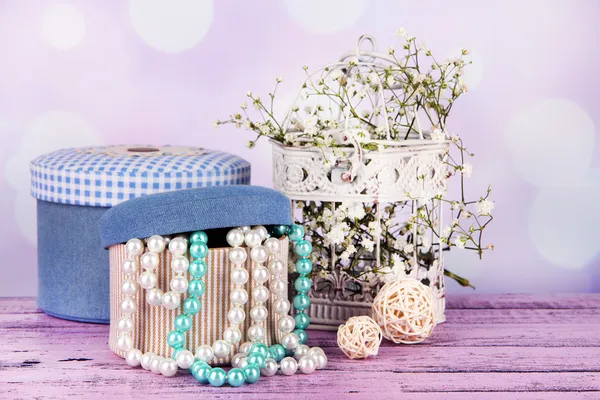 Boîtes décoratives avec des perles et des fleurs sur la table sur fond lumineux — Photo