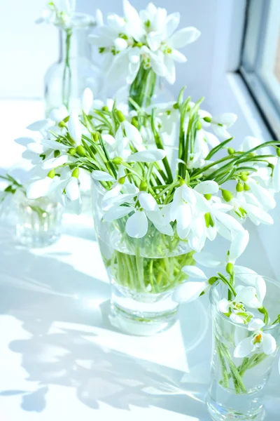 Beautiful bouquets of snowdrops in vases on windowsill — Stock Photo, Image