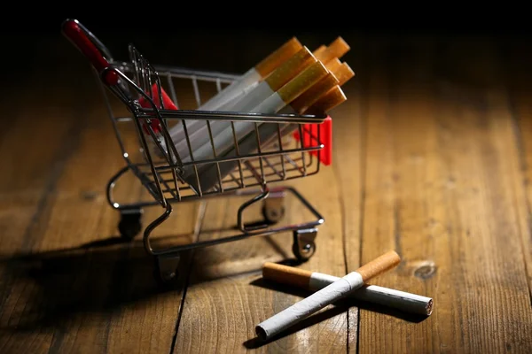 Cigarros no carrinho de compras na mesa de madeira no fundo escuro — Fotografia de Stock