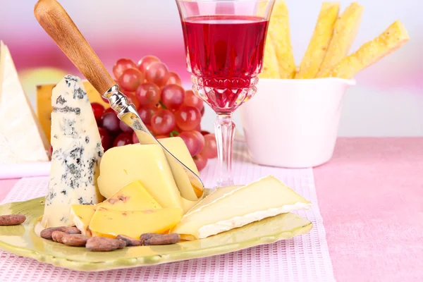 Placa de queso surtido, copa de uva y vino en la mesa, sobre fondo claro — Foto de Stock