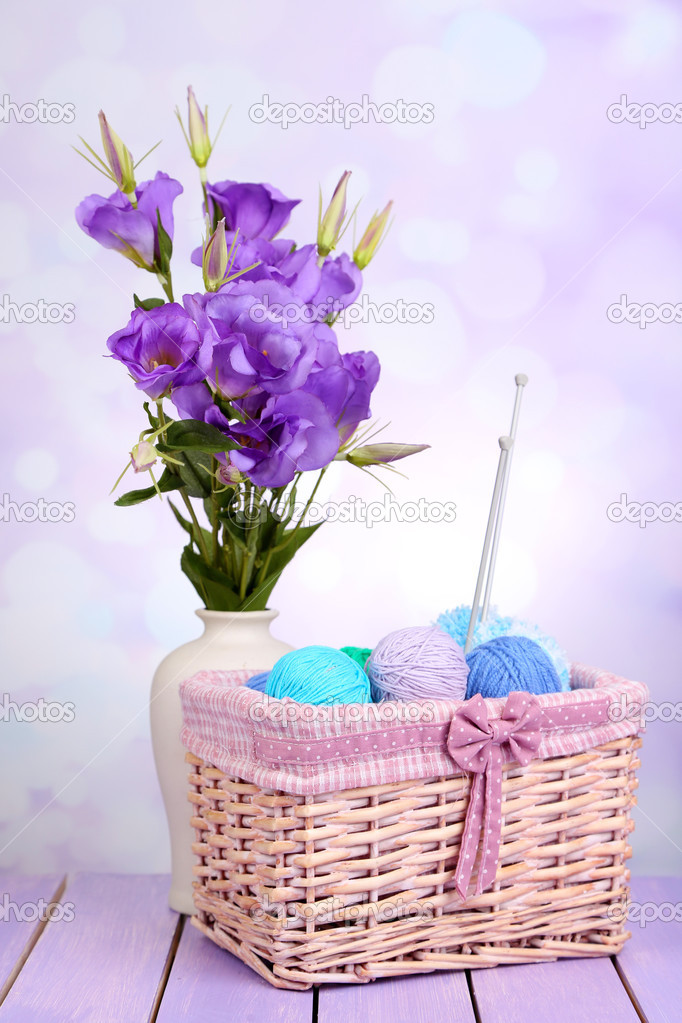 Purple artificial eustoma and woolen balls of yarn in basket on light background