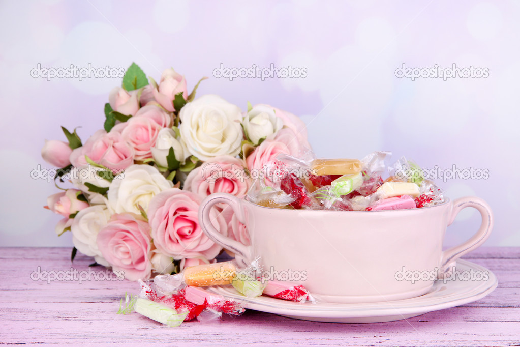 Tasty candies in bowl with flowers on table on bright background