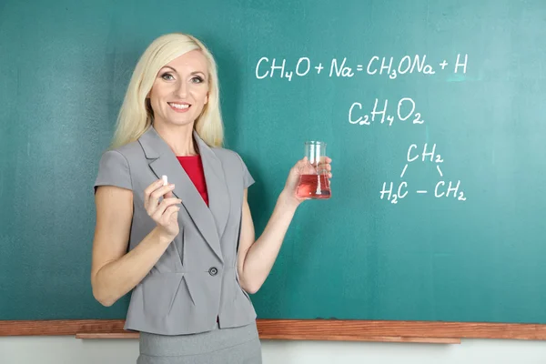 Young teacher writing chemical formula on blackboard — Stock Photo, Image