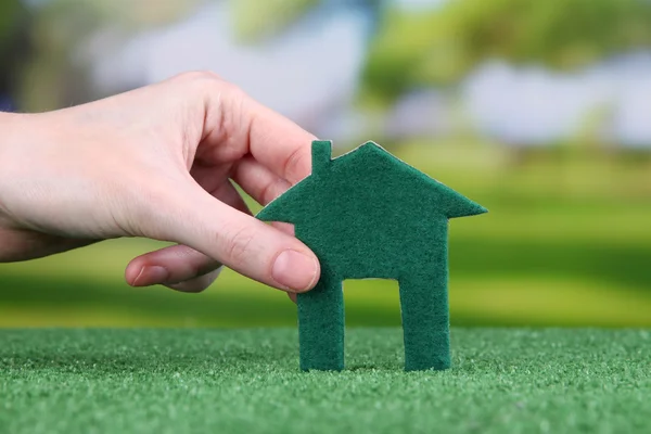 Lilla papper huset i handen på grönt gräs på ljus bakgrund — Stockfoto