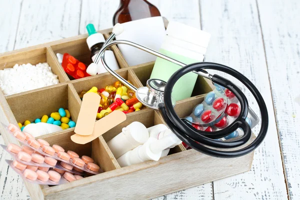 Медицинские таблетки, стетоскоп, ампулы в деревянной коробке, на фоне цвета дерева — стоковое фото