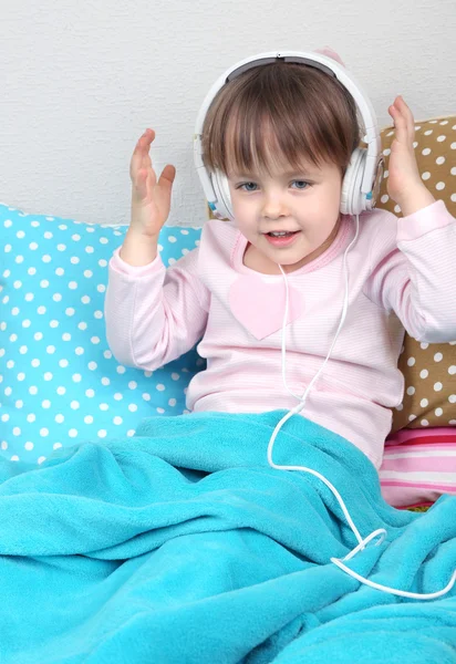 Little girl sitting on pillows on wall background — Stock Photo, Image