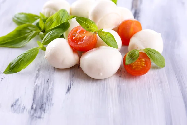 Tasty mozzarella cheese with basil and tomatoes, on wooden table — Stock Photo, Image