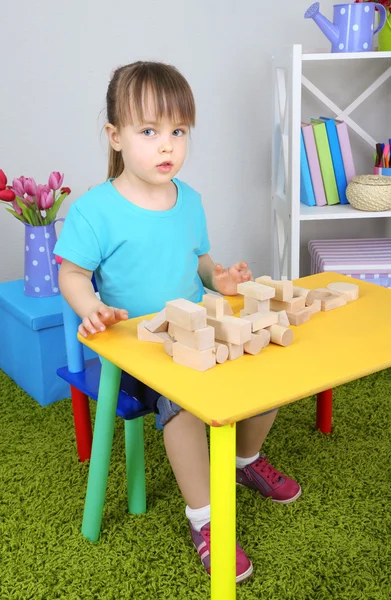 Little girl plays with construction blocks sitting at table in room — Stock Photo, Image