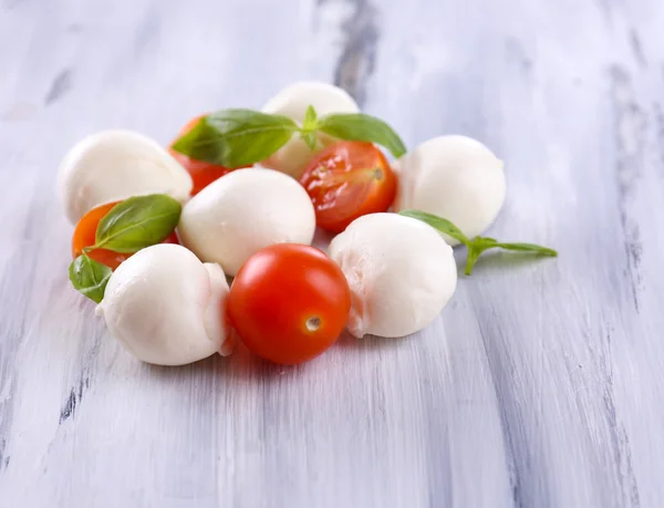 Tasty mozzarella cheese with basil and tomatoes, on wooden table — Stock Photo, Image