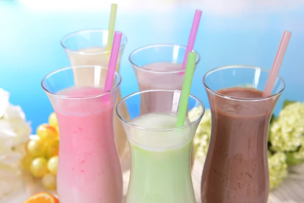 Melk schudt met vruchten op tafel op lichte blauwe achtergrond — Stockfoto