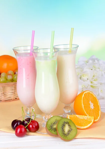 Milk shakes with fruits on table on light blue background — Stock Photo, Image