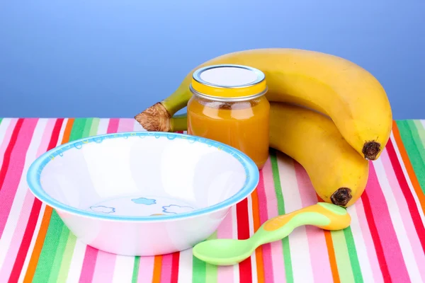 Jar of baby puree with plate and spoon on napkin on blue background — Stock Photo, Image