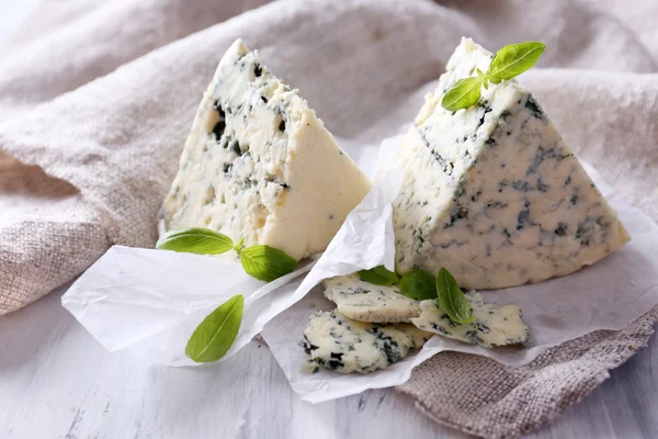 Smakelijke blauwe kaas met basilicum op papier — Stockfoto
