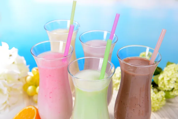 Frullati di latte con frutta sul tavolo su sfondo azzurro — Foto Stock