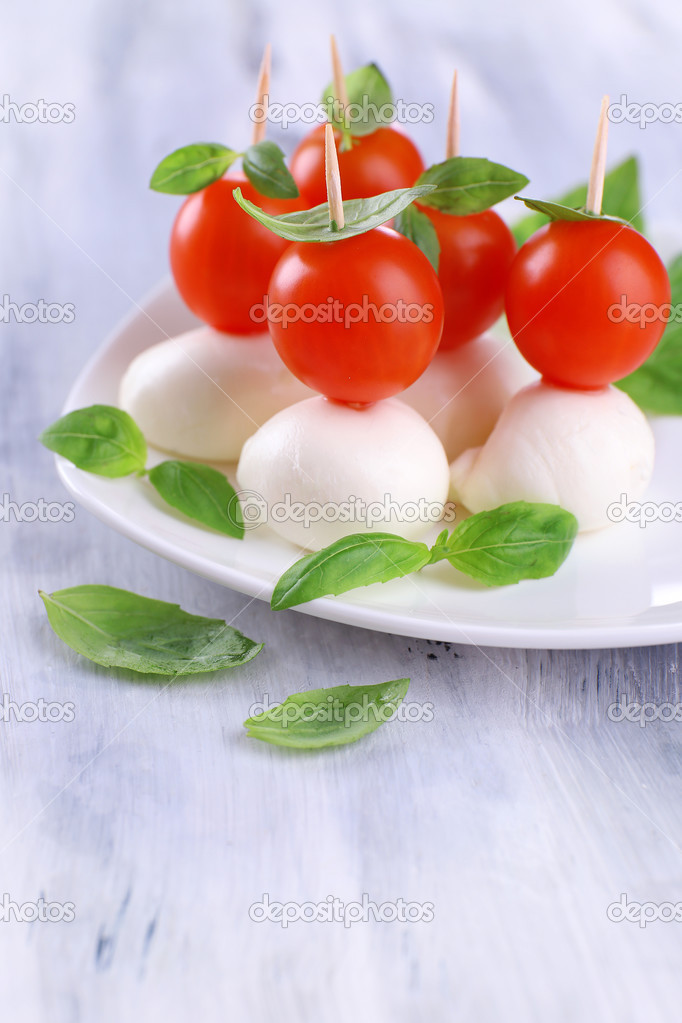 Tasty mozzarella cheese with basil and tomatoes on plate, on wooden table