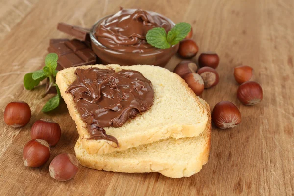 Roti dengan coklat manis hazelnut menyebar di latar belakang kayu — Stok Foto