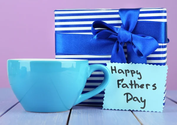 Happy Fathers Day tag with gift box and cup, on wooden table, on light background — Stock Photo, Image