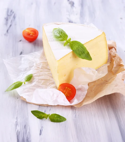 Tasty Camembert cheese with basil and tomato, on wooden table — Stock Photo, Image