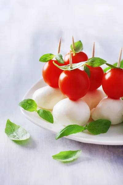 Tasty mozzarella cheese with basil and tomatoes on plate, on wooden table — Stock Photo, Image