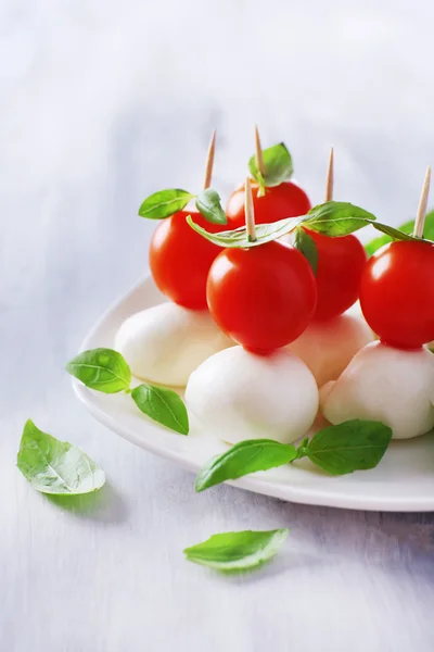 Välsmakande mozzarellaost med basilika och tomater på plattan, träbord — Stockfoto