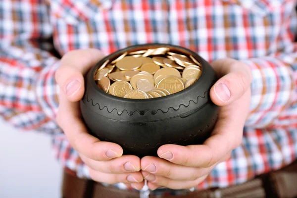 Keramische pot met gouden munten in mannelijke handen, op lichte achtergrond — Stockfoto