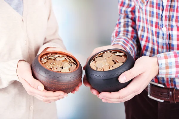 Twee keramische potten met gouden munten in mannelijke en vrouwelijke handen, op lichte achtergrond — Stockfoto