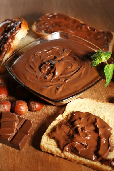 Sladká čokoláda lískových spread s celých skořápkových plodech a mincovna na dřevěné pozadí — Stock fotografie