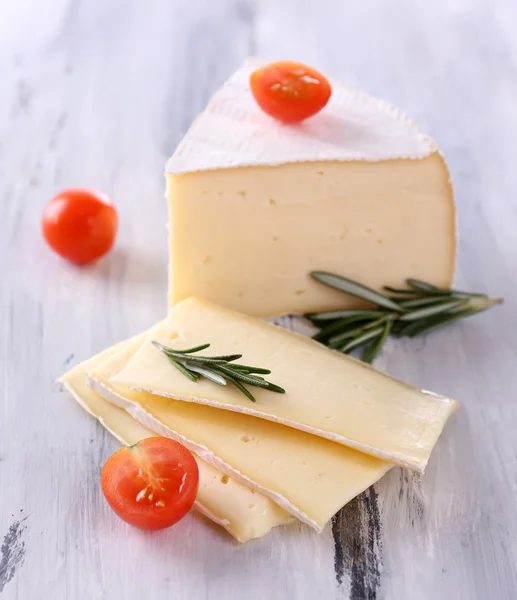 Tasty Camembert cheese with tomato and rosemary, on wooden table — Stock Photo, Image