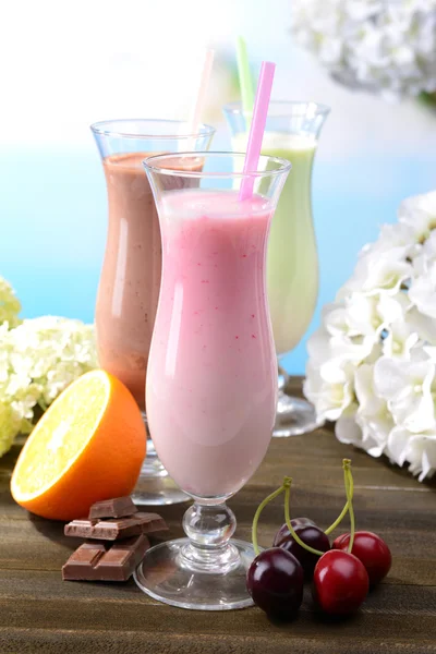 Melk schudt met vruchten op tafel op lichte blauwe achtergrond — Stockfoto