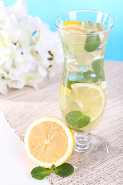 Glass of cocktail with lemon and mint on table on light blue background — Stock Photo, Image