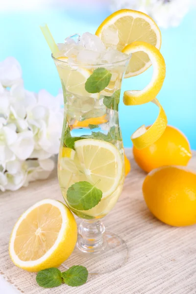 Glass of cocktail with lemon and mint on table on light blue background — Stock Photo, Image