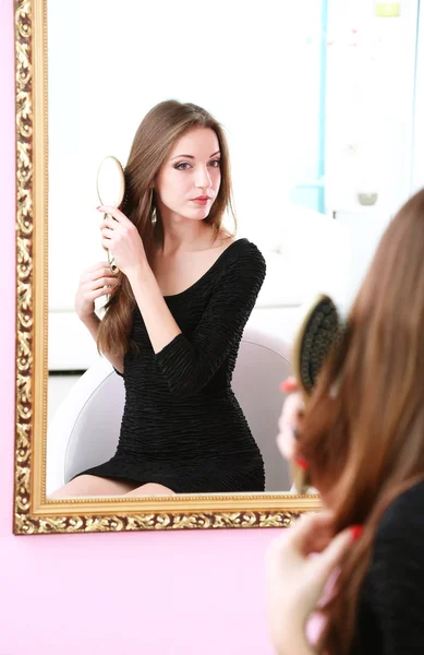 Young beautiful woman making hairstyle near mirror — Stock Photo, Image